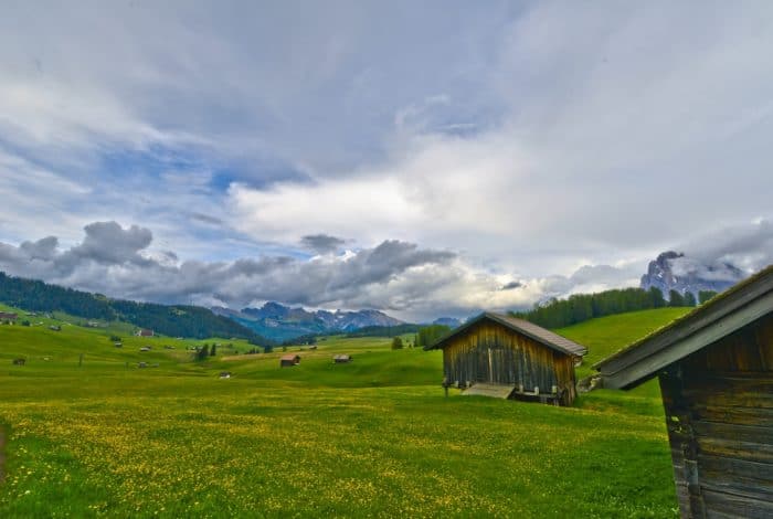 brown wooden house on green grass field under white clouds and blue sky during daytime